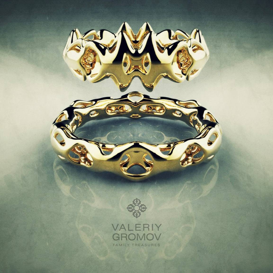Two gold rings with intricate designs on a reflective surface, featuring the brand 'Valeriy Gromov'.