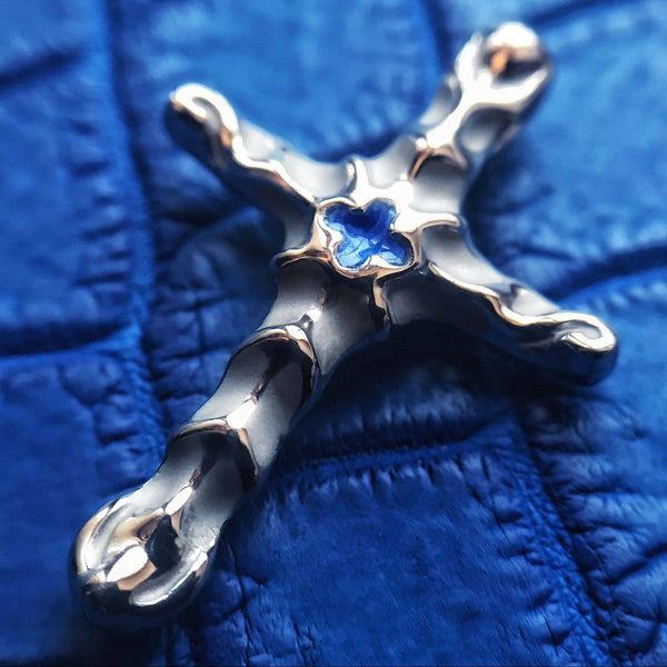 Handcrafted platinum cross pendant with fluid, molten edges and a cobalt-blue hot-enamel centerpiece, photographed close-up on a rich blue background — modern luxury crucifix by GROMOV