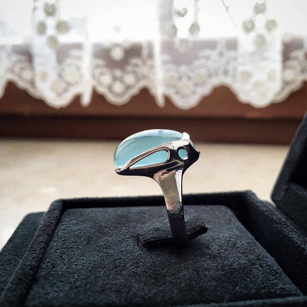 white gold ring with a blue aquamarine on a black cushion, lace curtain in the background