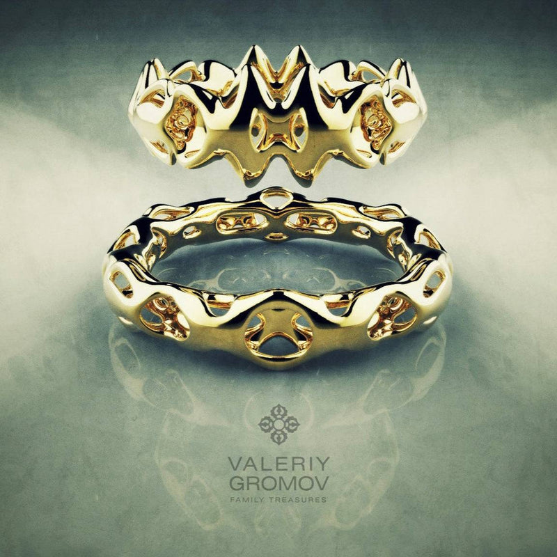 Two gold rings with intricate designs on a reflective surface, featuring the brand 'Valeriy Gromov'.