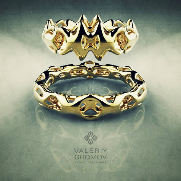 Two gold rings with intricate designs on a reflective surface, featuring the brand 'Valeriy Gromov'.