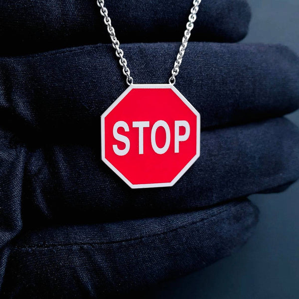 Red 'STOP' sign white gold pendant on a chain against a dark background