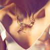 Woman wearing a yellow-gold Tyrannosaur NEX necklace—an articulated T-rex skeleton draped across her collarbone in warm summer light.